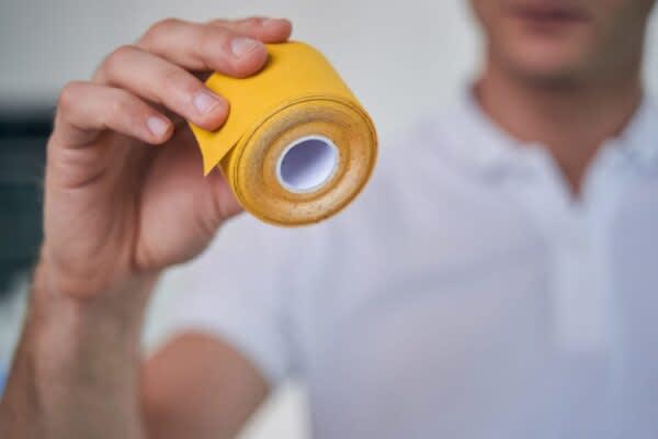 Mouth Tape for Sleep A man's hand holding bright yellow kinesiology tape.