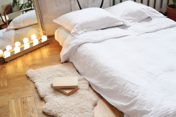 An air mattress placed in the floor with linens on top of it. A mirror stands beside the air mattress with vanity lights in front of it.