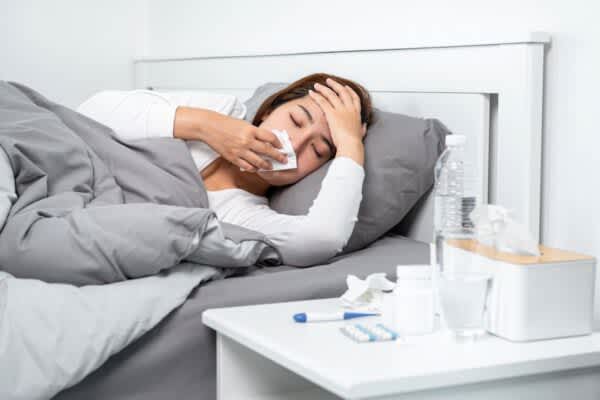 COVID-19 and Sleep: Everything You Need to Know stock photo of a sick woman blowing her nose while lying in bed