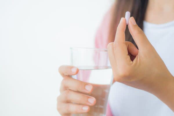 Melatonin Dosage stock photo of a woman holding a pill and a glass of water