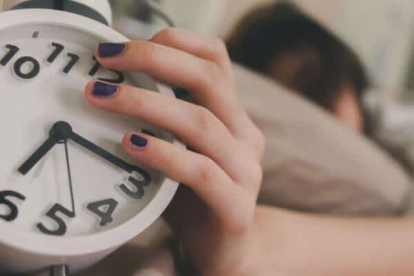 How Many Hours of Sleep Do We Need? stock photo of a person holding a clock