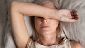 Close up top view of a middle aged woman resting in bed with her arm over her eyes