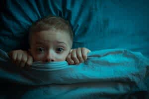 stock photo of a frightened child peaking from underneath the blanket