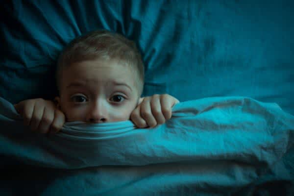 What Causes Nightmares? stock photo of a frightened child peaking from underneath the blanket