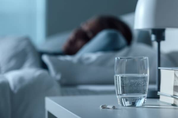 Magnesium for Sleep Woman asleep in bed with a glass of water and a sleep aid on the night stand.