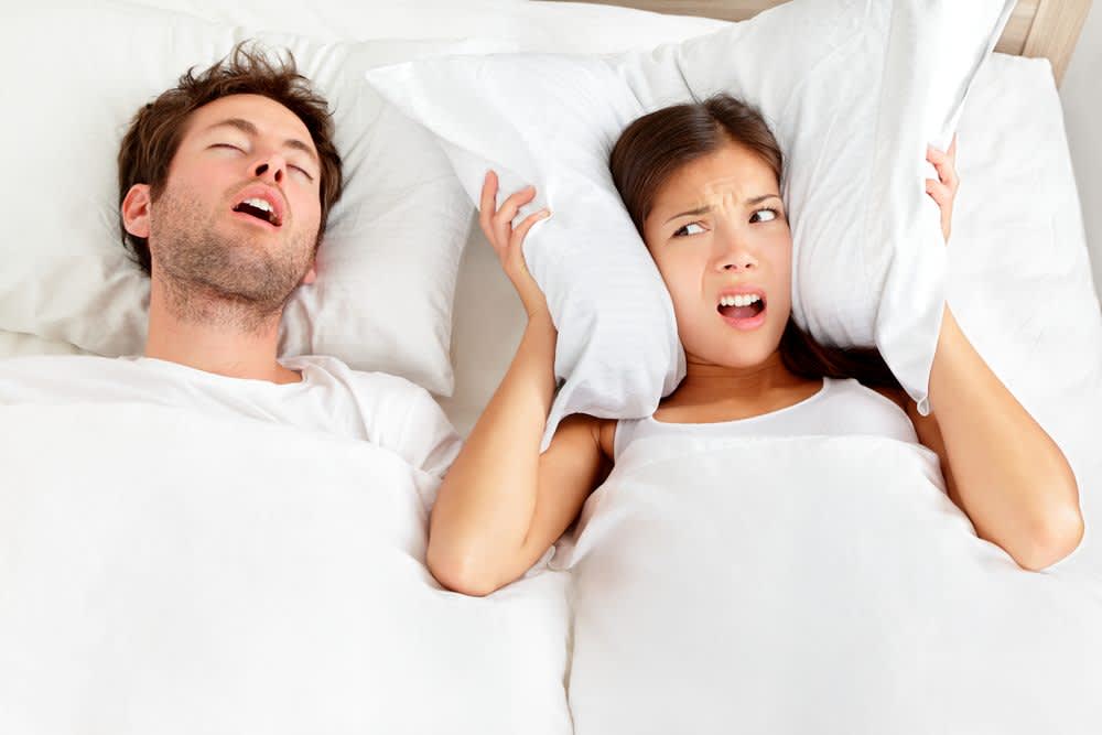 How to Stop Snoring stock image of a woman covering her ears with a pillow because of her partner's snoring