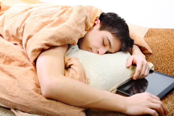 Teens and Sleep: What to Know About Healthy Rest Tired teenager sleeping on the bed with tablet computer